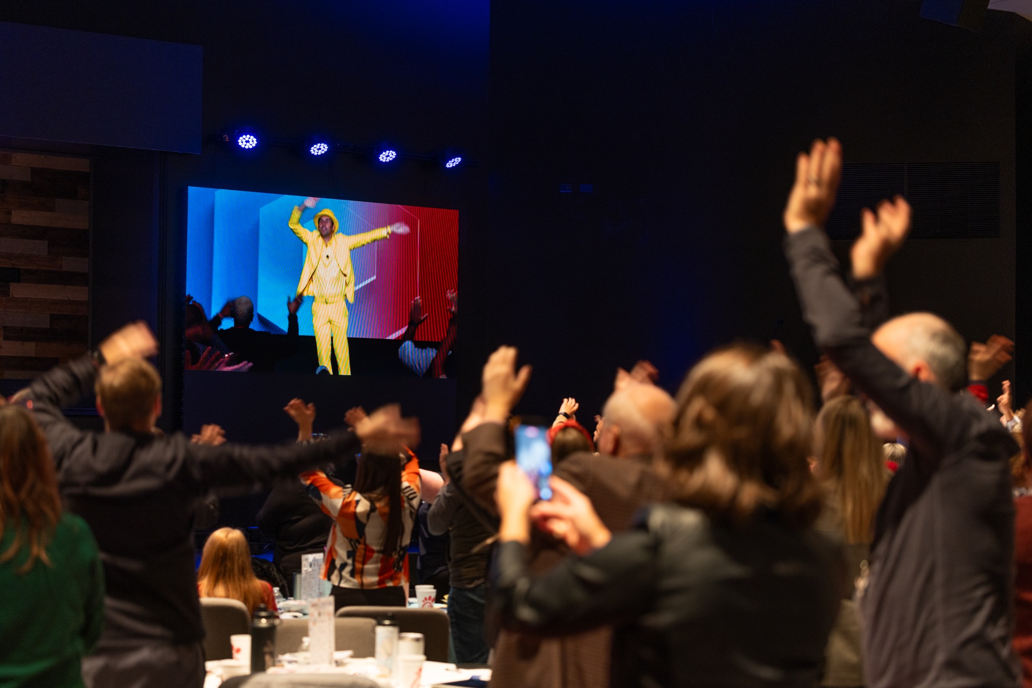 Attendees raising their hands during a recorded presentation on the event screen