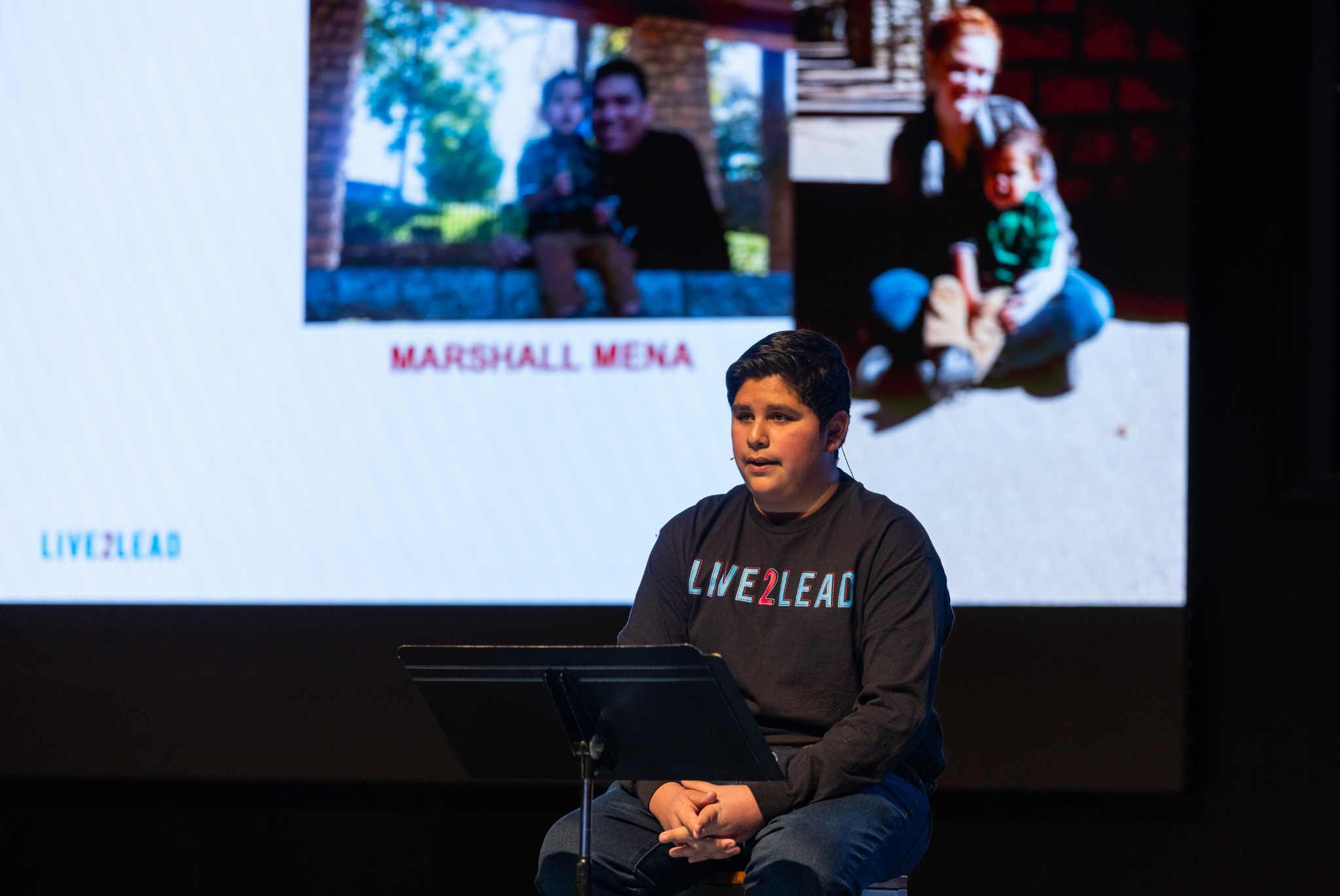 A young speaker sharing his story onstage with family photographs on the screen