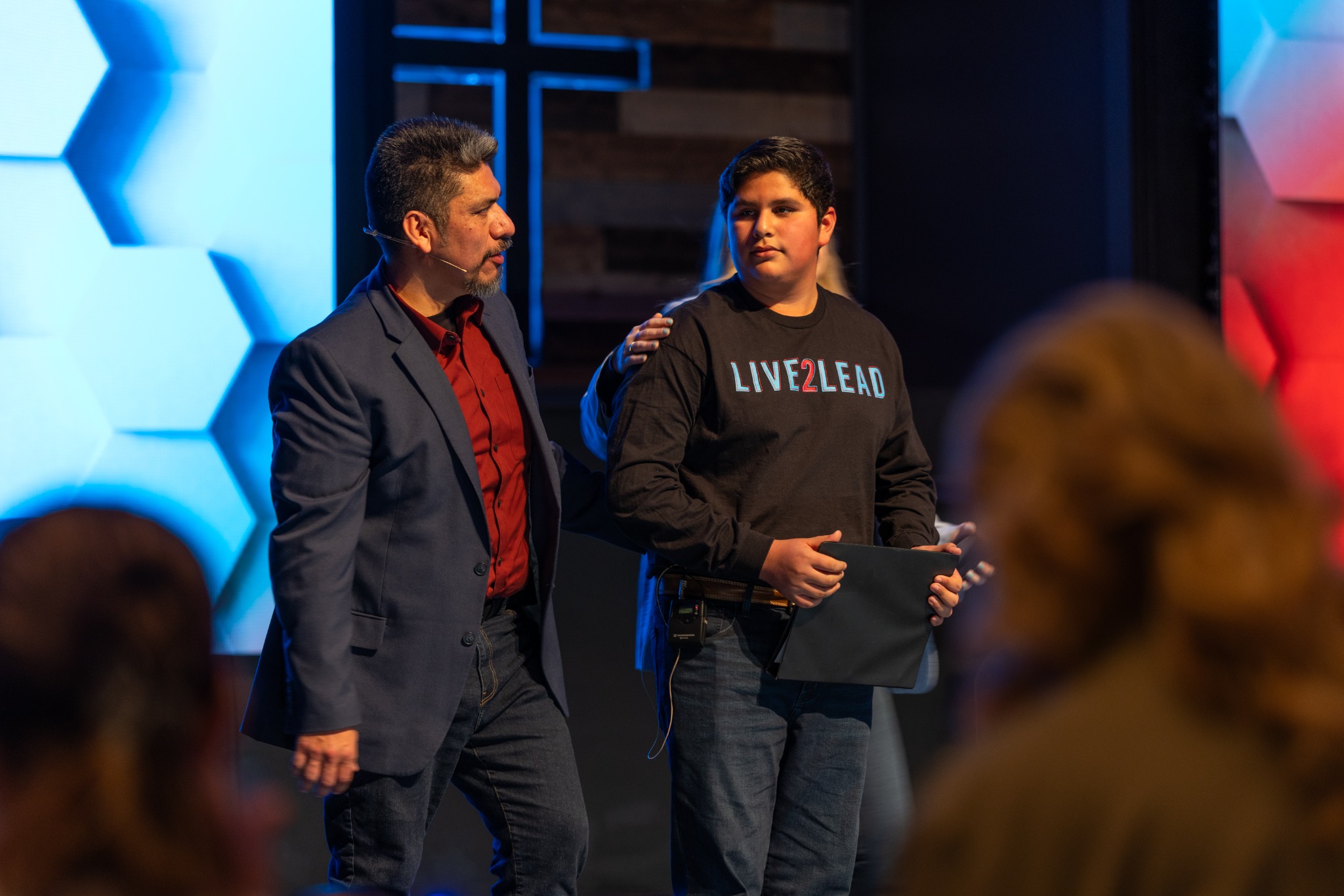 Heber Mena standing beside a young speaker on the Live2Lead stage