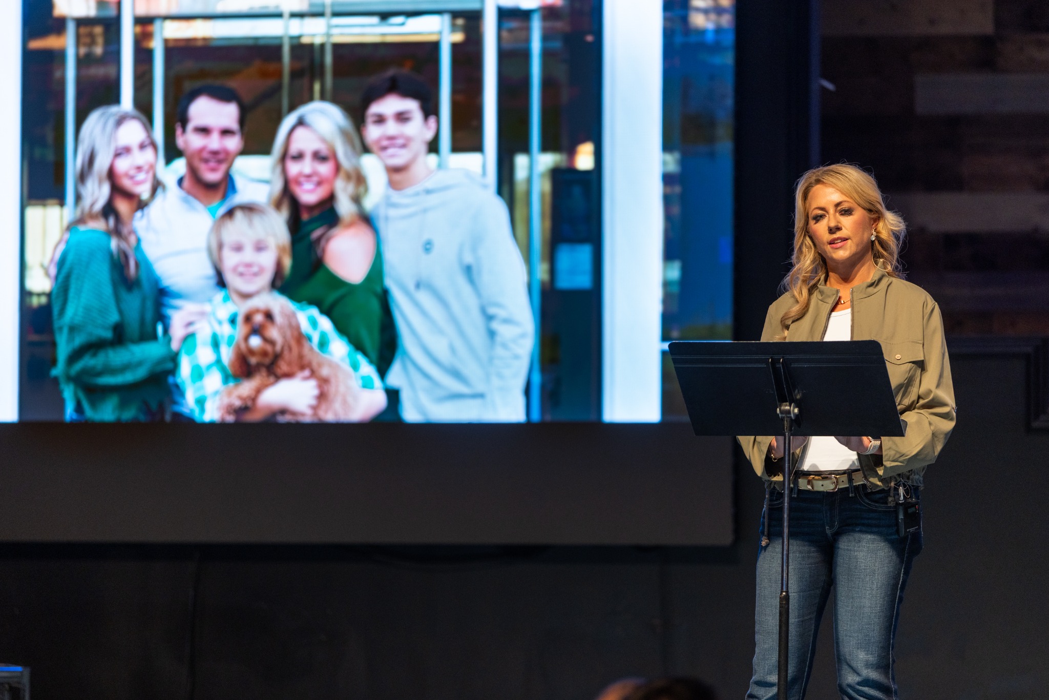 A speaker presenting onstage beside a family photograph