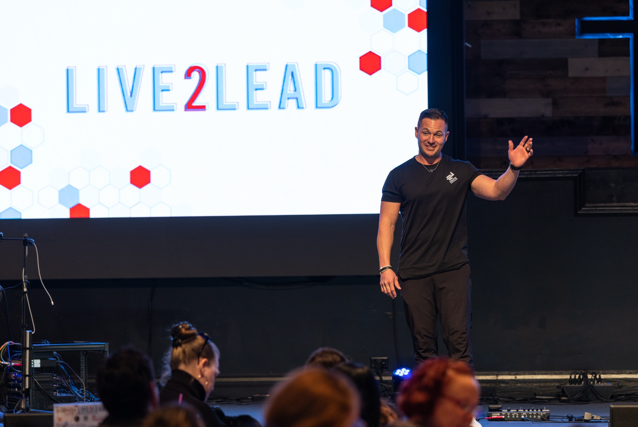 A speaker gesturing to the audience beside the Live2Lead screen