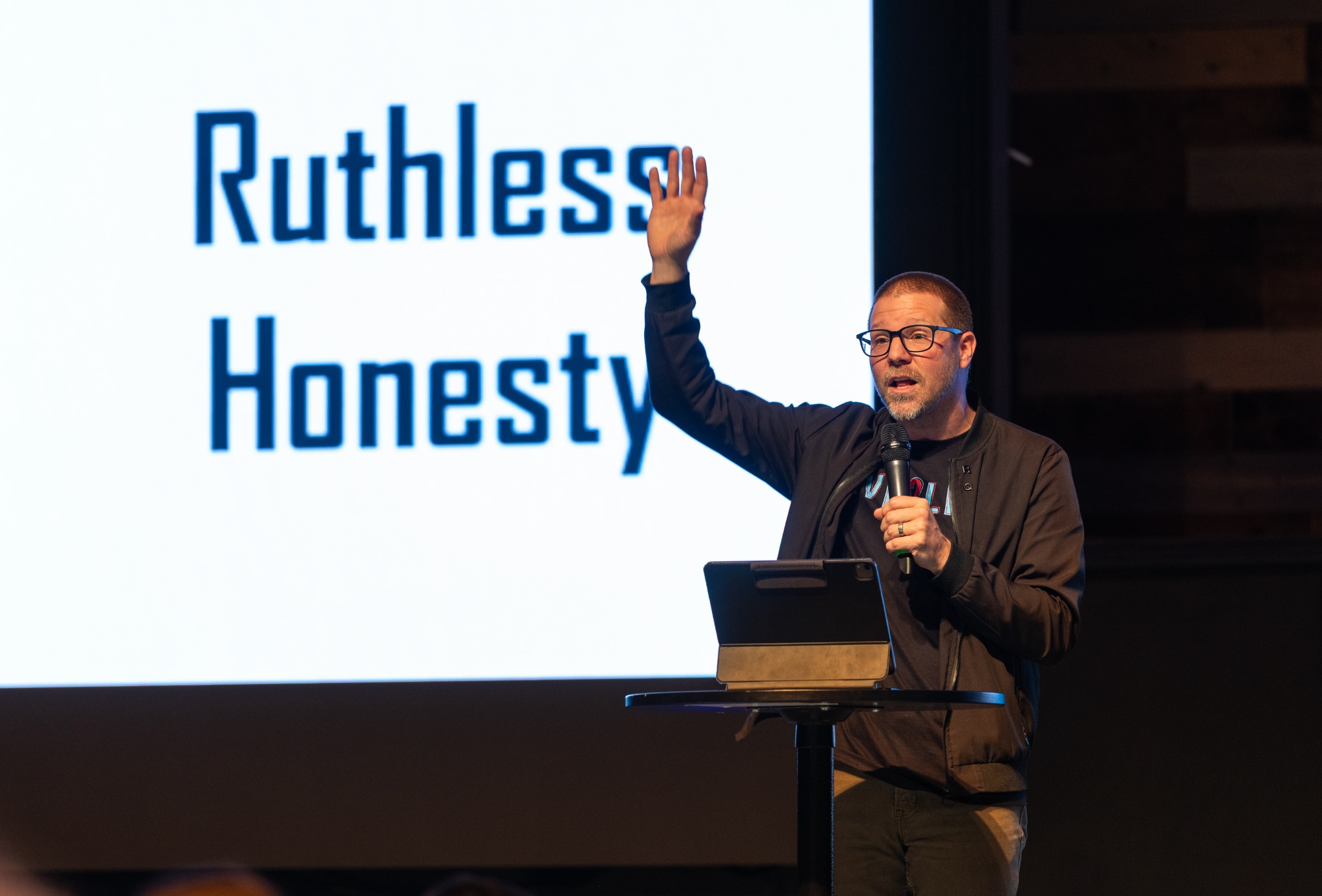 A speaker with a microphone presenting beside a slide about honesty